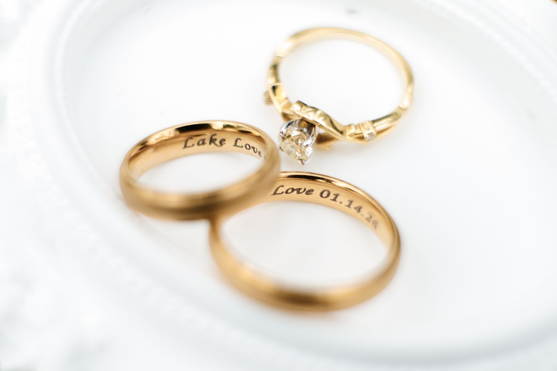 Three gold rings on a white surface, two engraved with “Love”