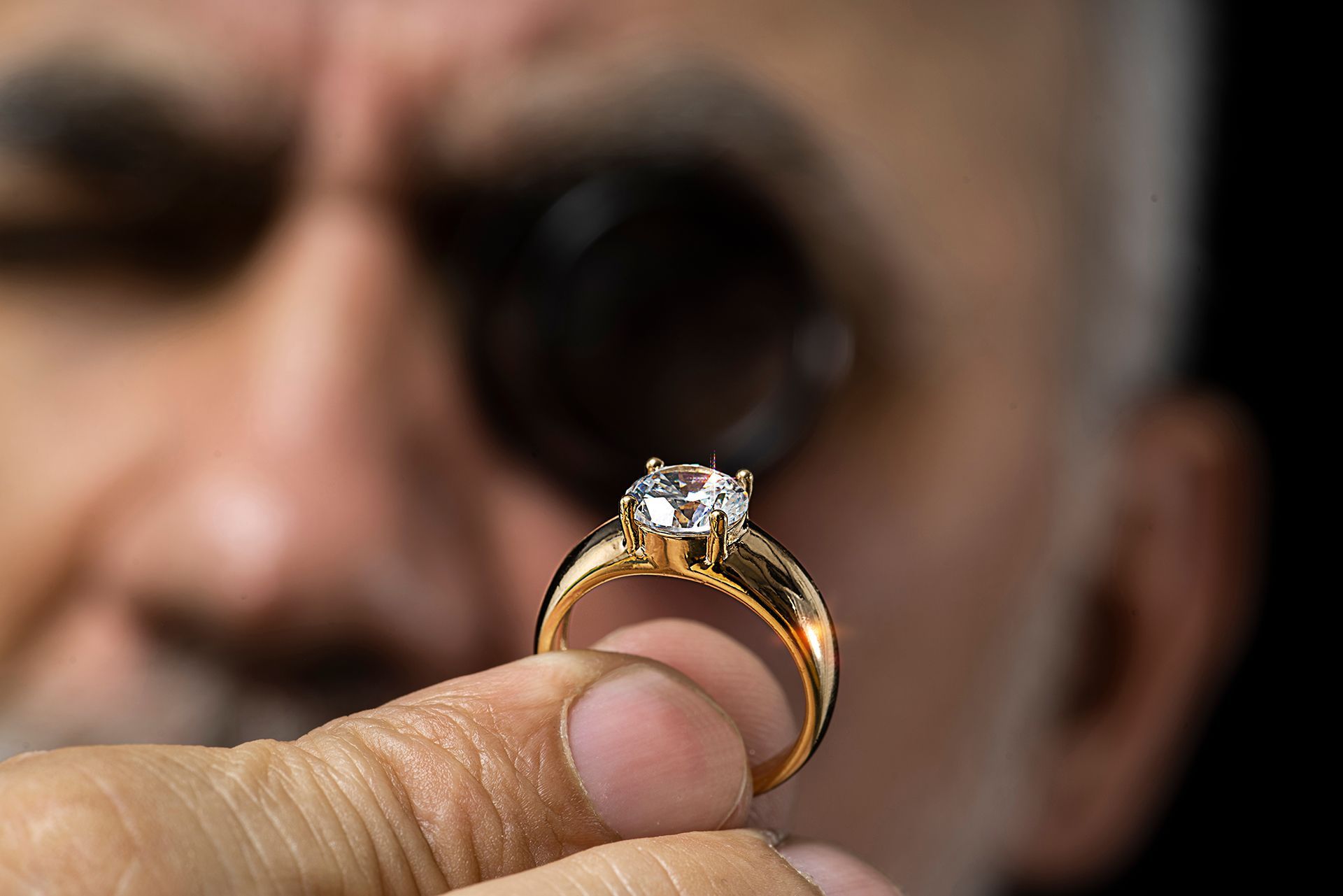 Hand holding a gold ring with a diamond, with a blurred face in the background