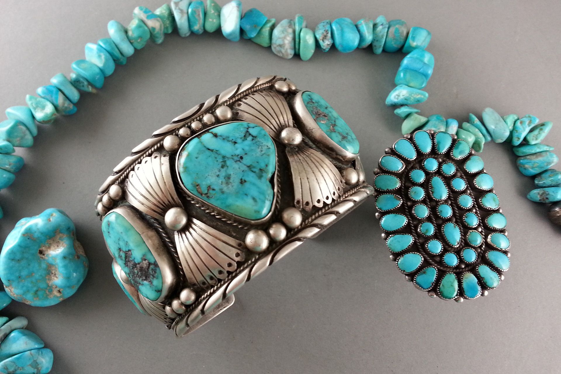 Turquoise and silver Native American-style jewelry: necklace, ring, and bracelet on gray background