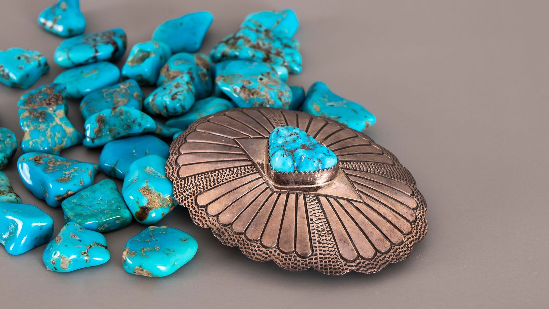 Turquoise stones scattered beside a copper medallion with a turquoise center on a beige surface
