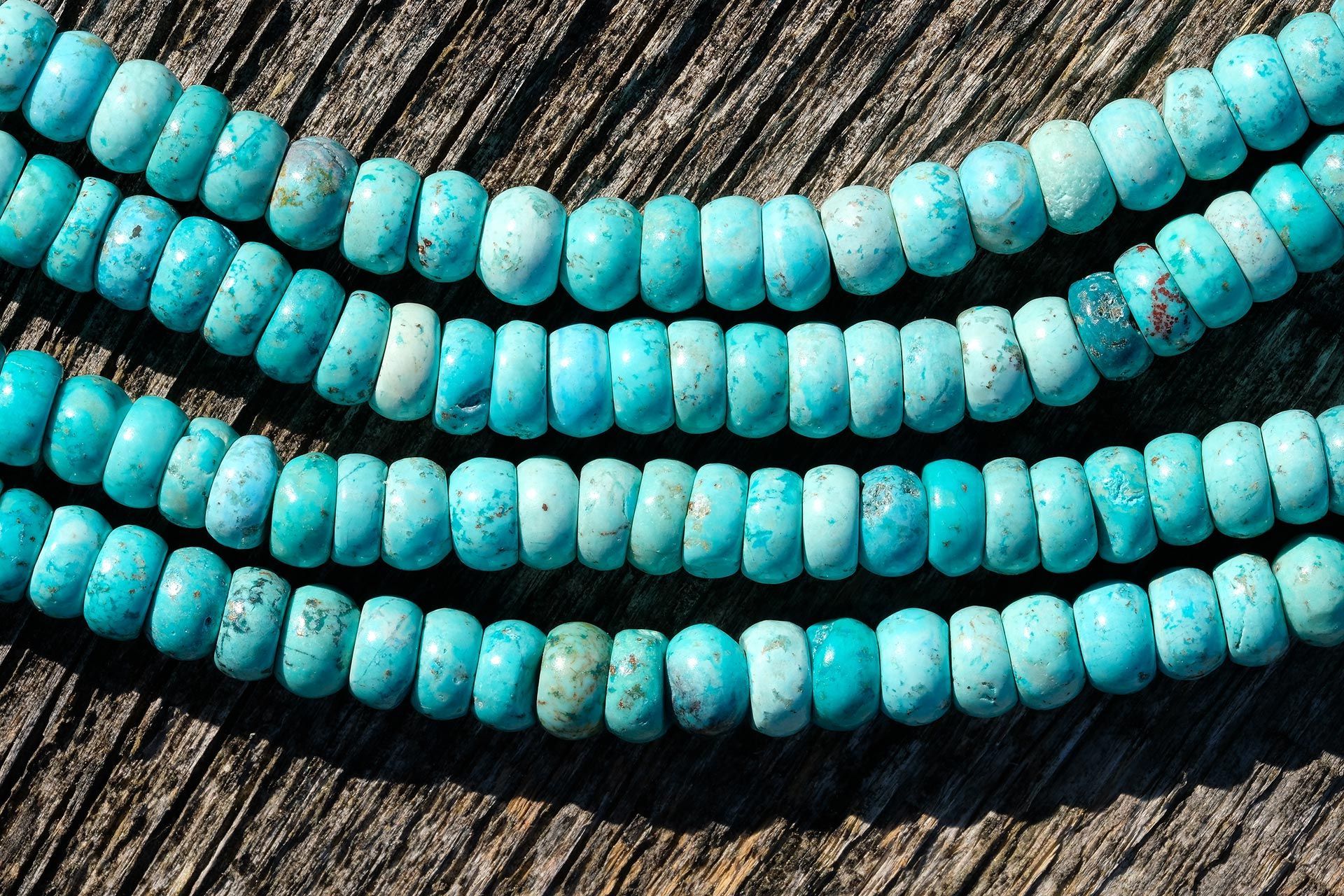Four strands of turquoise beads laid in curved rows on a dark wooden surface
