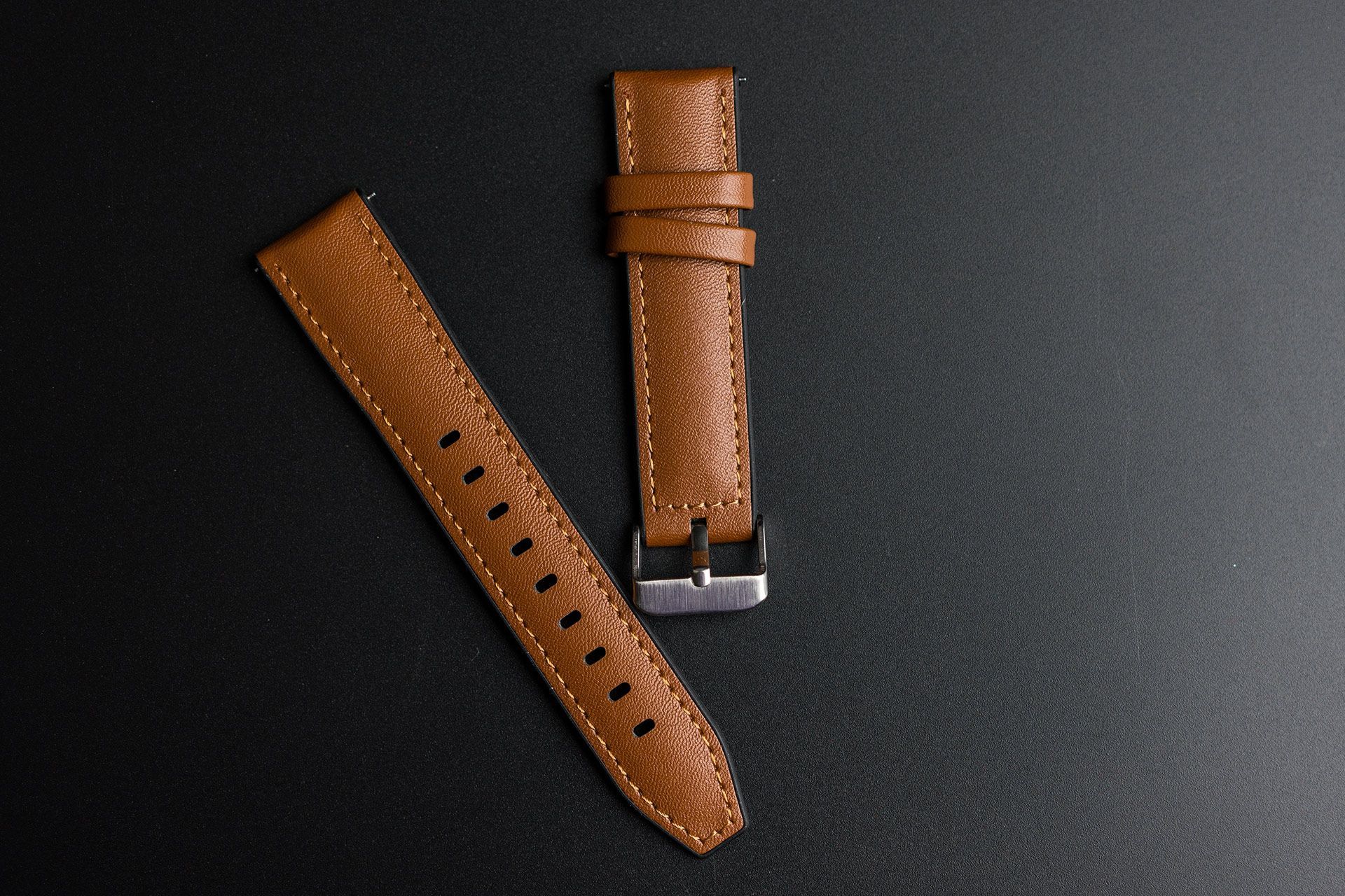 Two brown leather watch straps on a dark background, one with holes and one with a metal clasp.