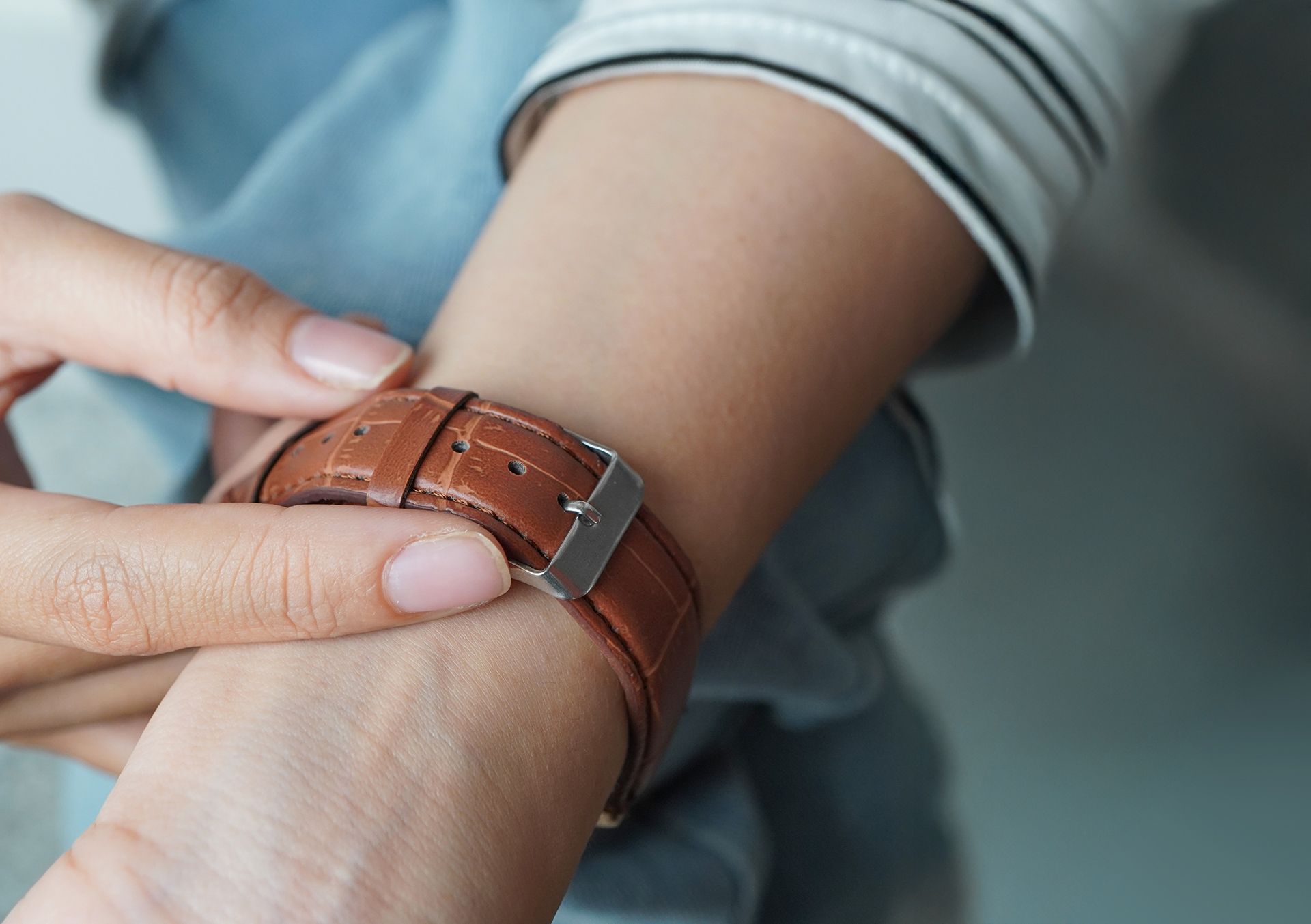 Hand fastening a brown leather wristwatch on a person's arm