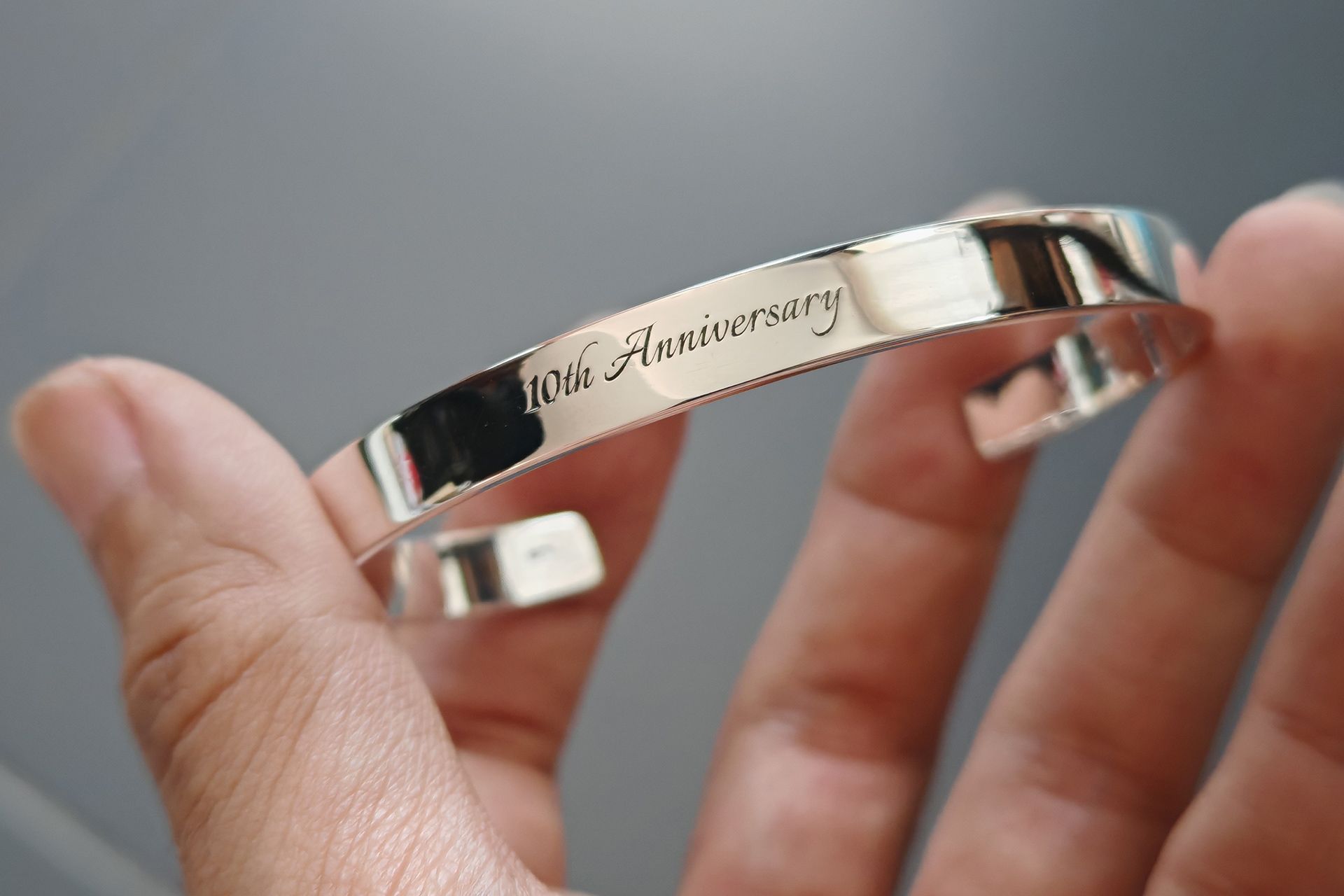 Hand holding a silver bracelet engraved “50th Anniversary”