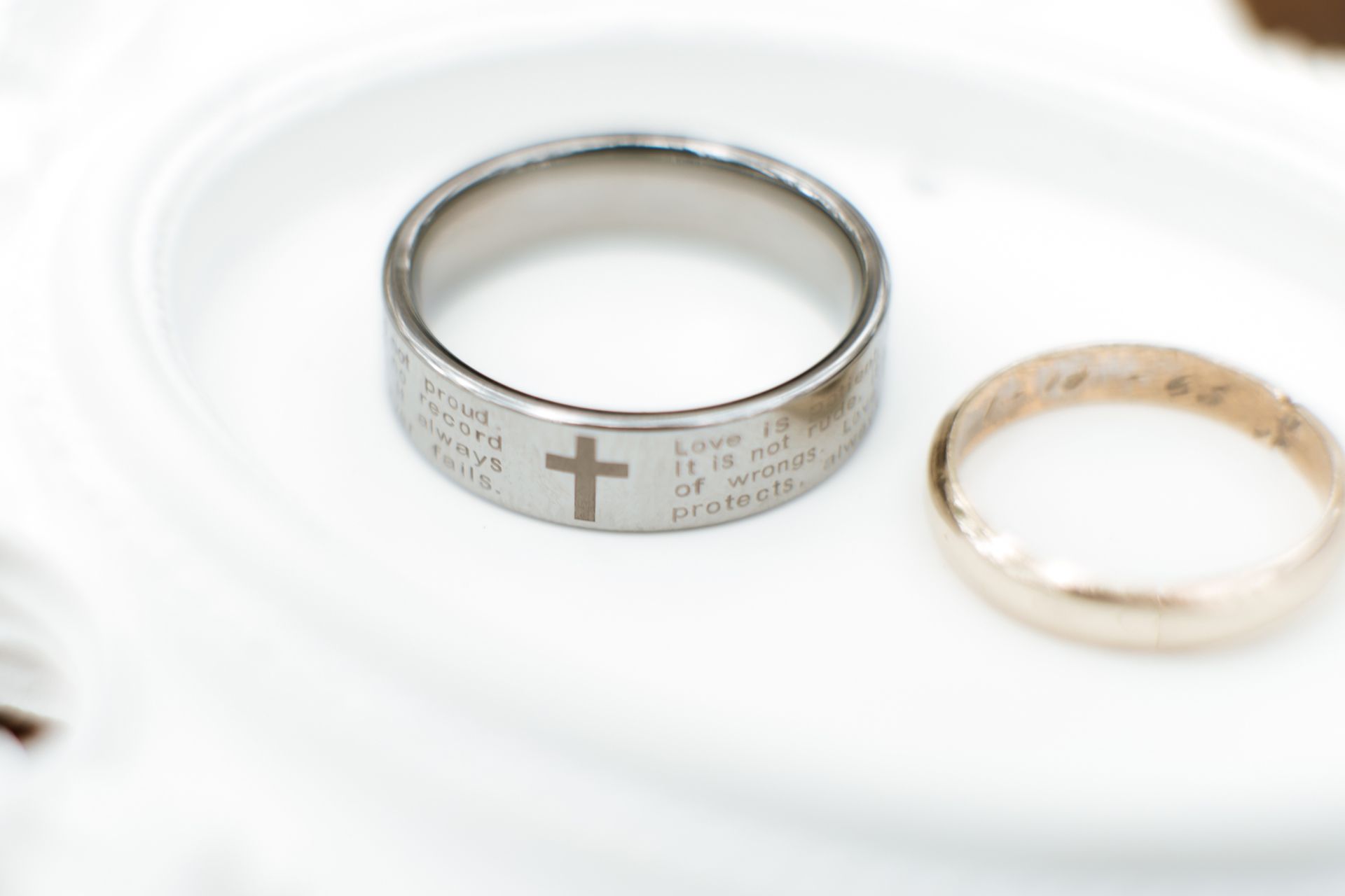 Two rings on a white surface, one silver with a cross and inscriptions, one gold-toned