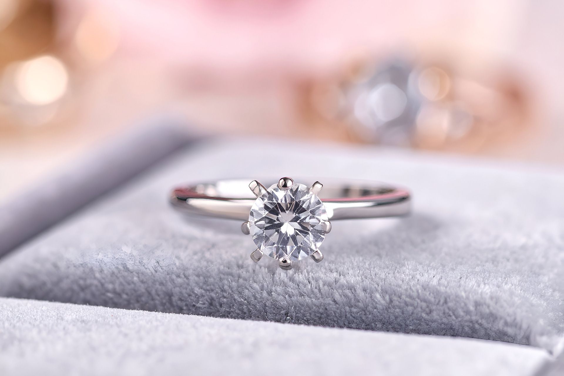Silver engagement ring with a clear gemstone on a gray velvet cushion