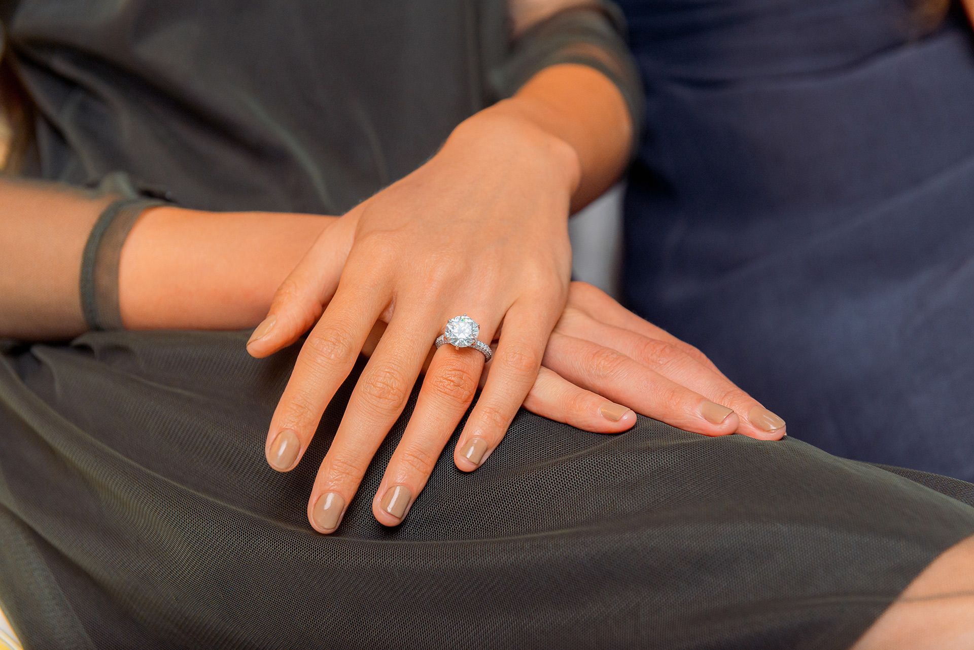 Close-up of hands resting on a lap, showing a blue gemstone ring and black clothing