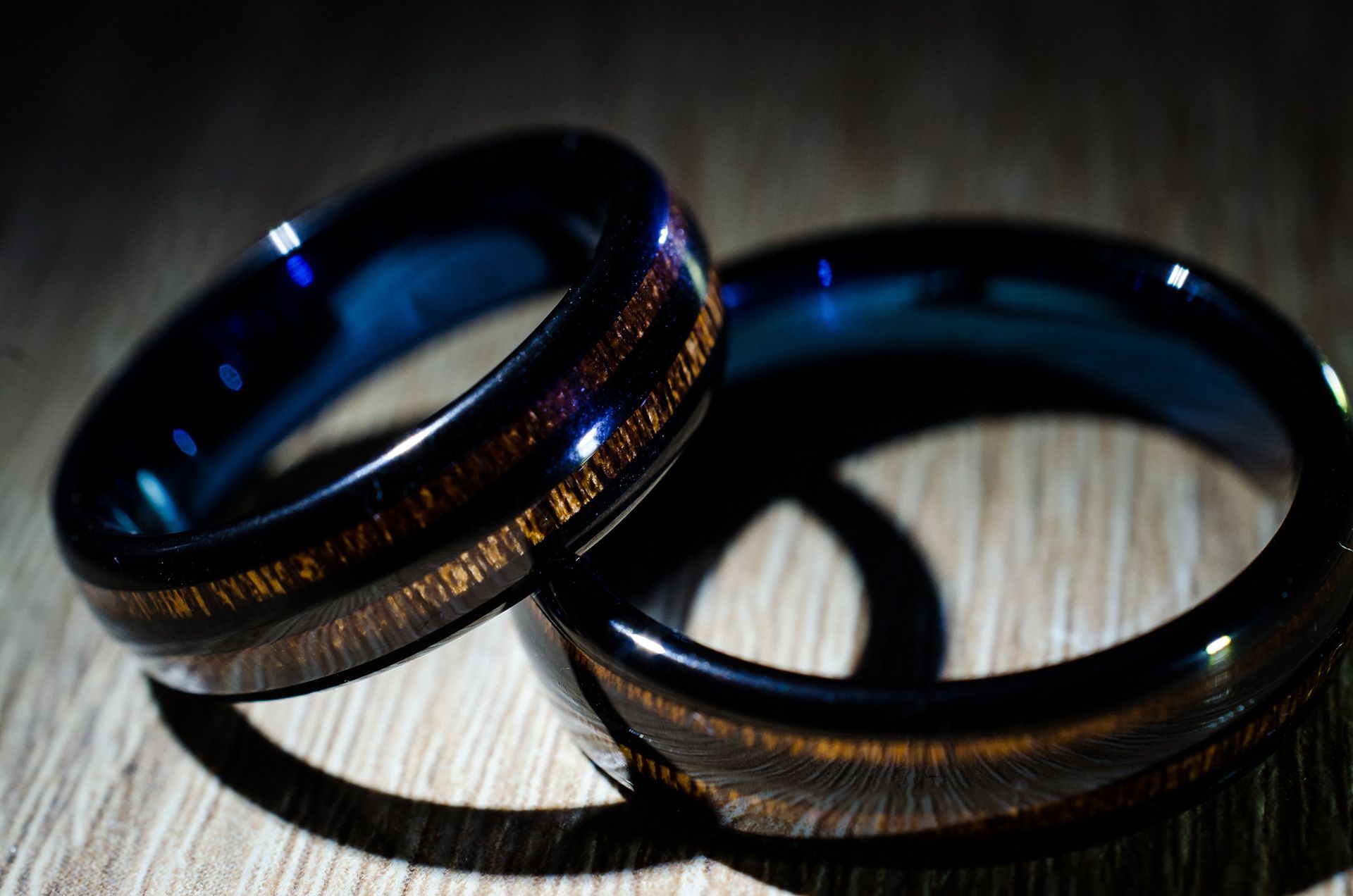 Two dark wedding bands resting on a light wood surface in soft shadow