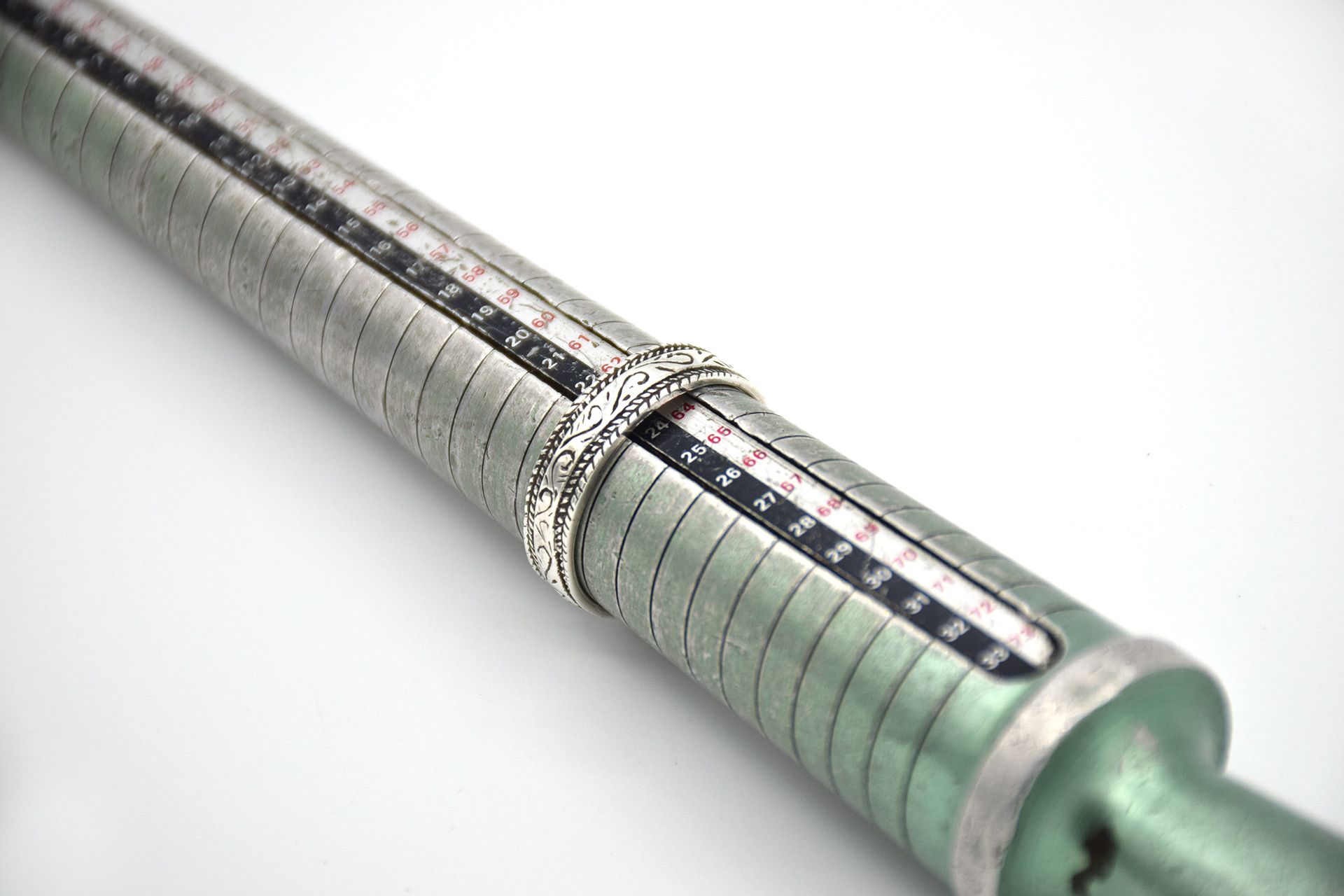 Close-up of a metallic cylindrical tool with measurement markings and a ring, on a white background