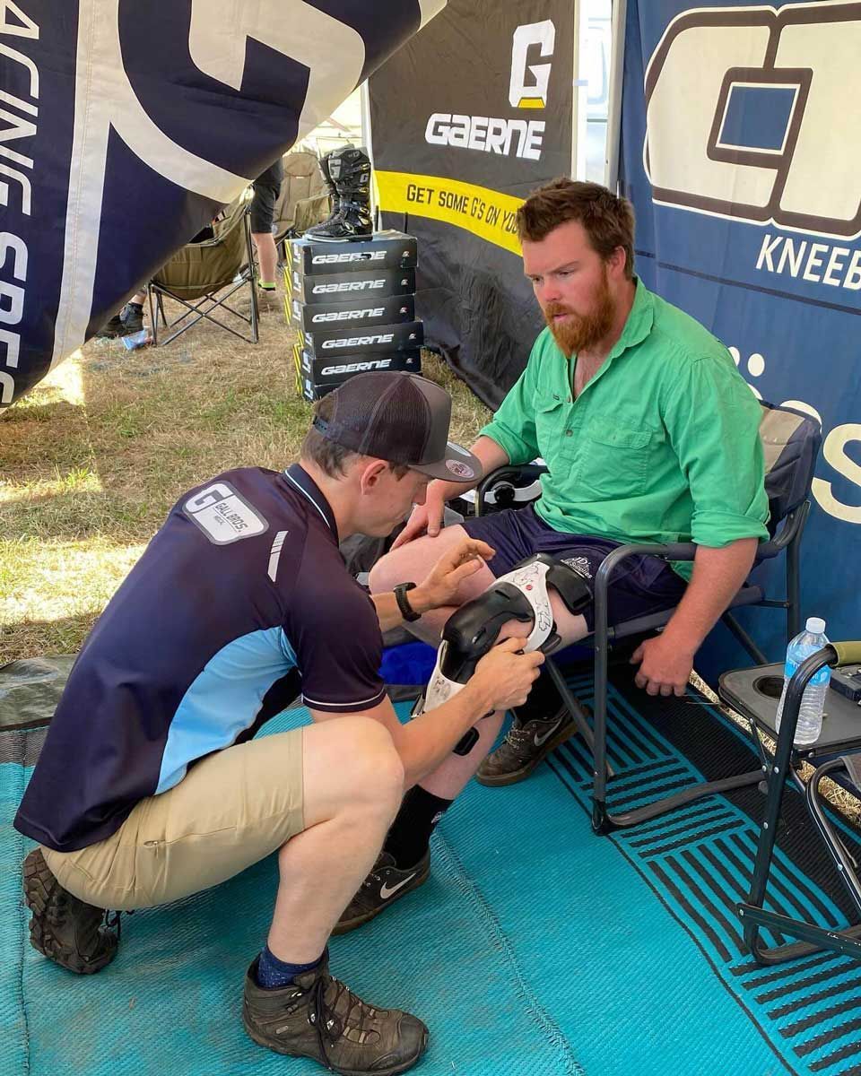A Man in a Green Shirt is Getting a Knee Brace on His Leg — Gall Bros Medical in Robina, QLD