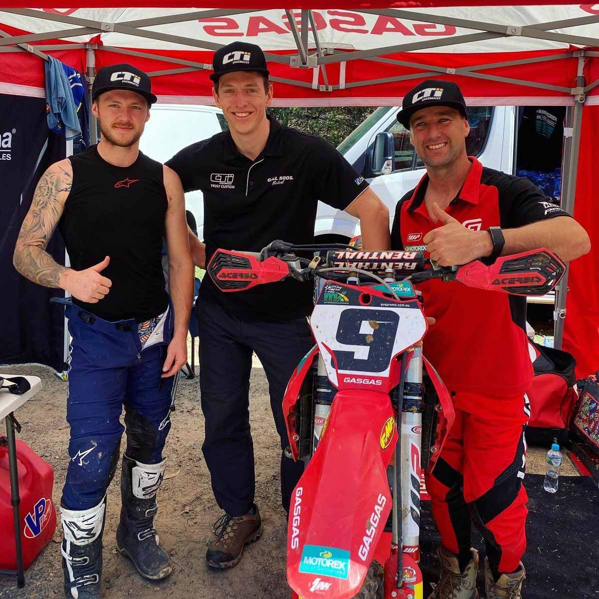 Three Men Standing Next to a Red Dirt Bike — Gall Bros Medical in Robina, QLD