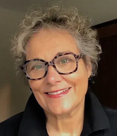 A woman wearing glasses and a black shirt is smiling for the camera.