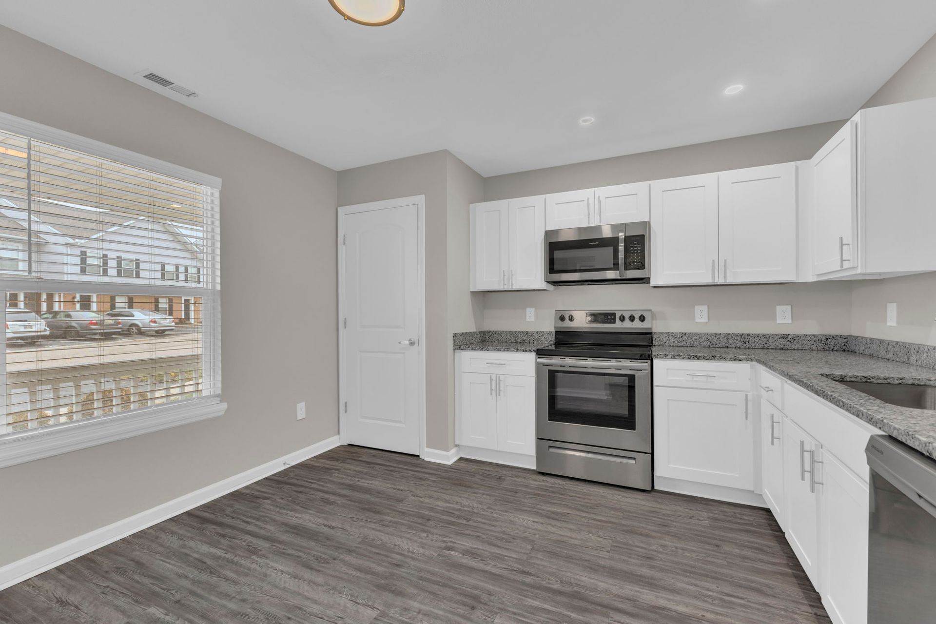 Kitchen with white cabinets, stainless steel appliances, gray countertops and flooring, and a window.