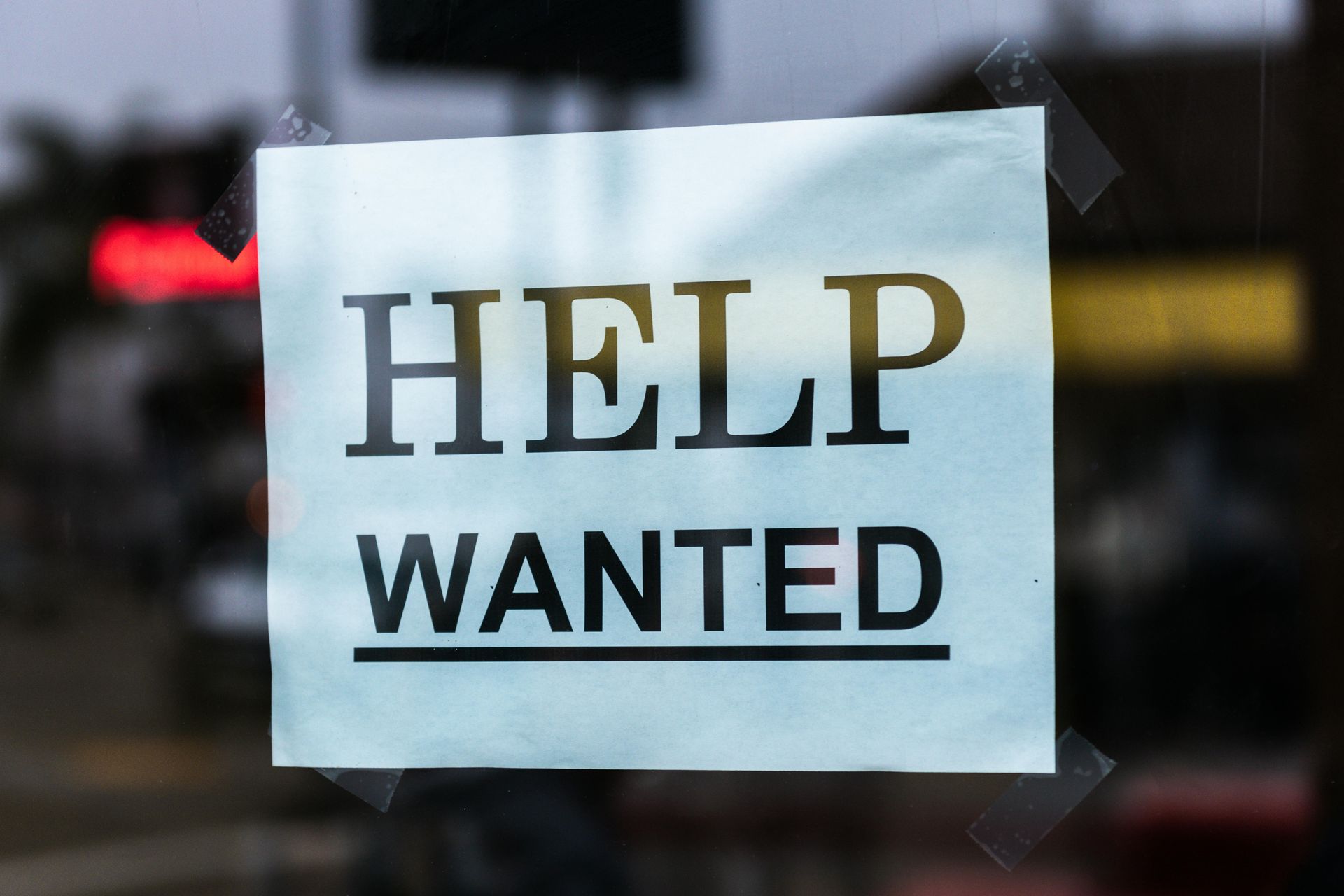 White “HELP WANTED” sign taped to a window.