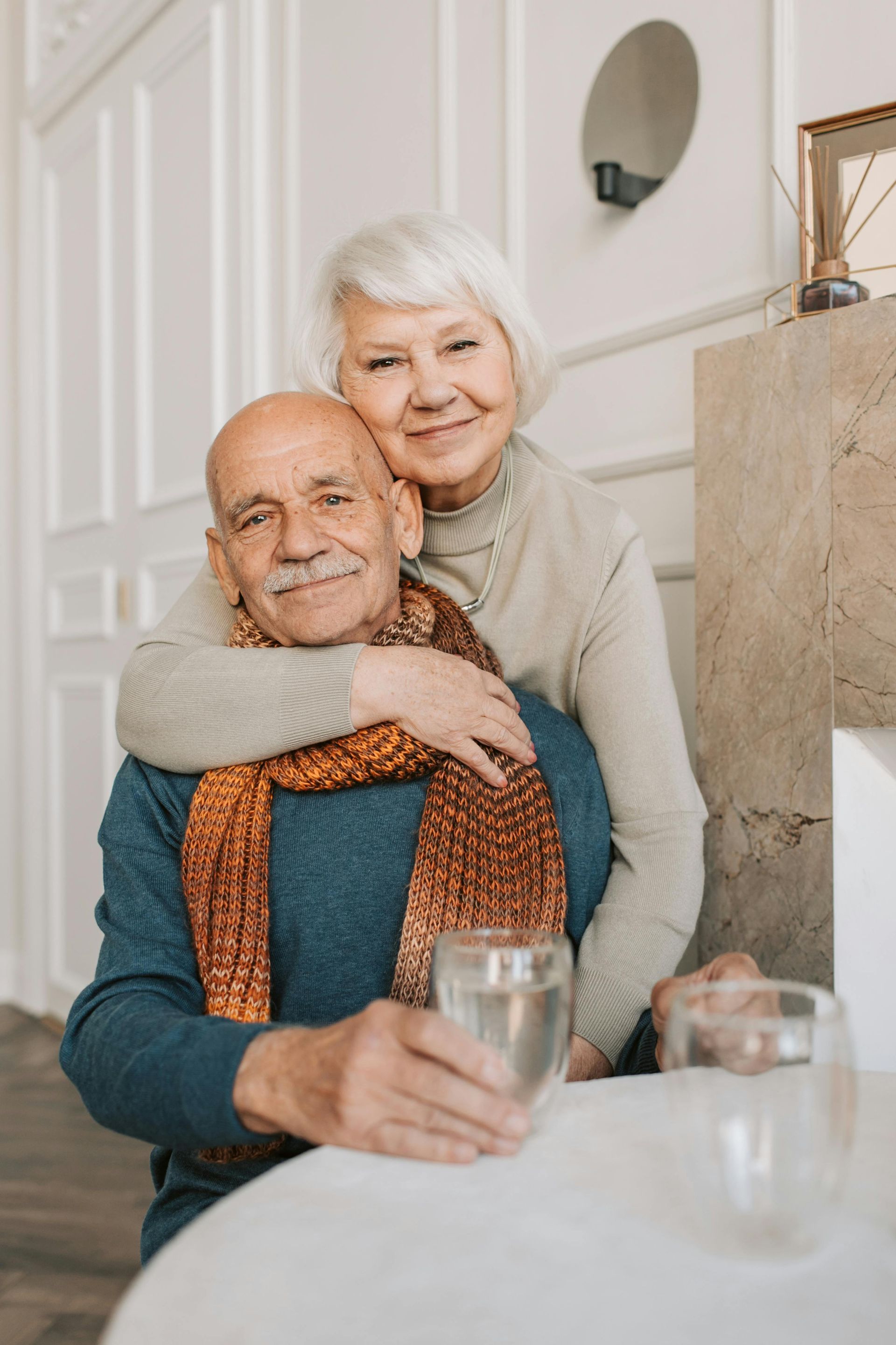 Smiling couple seated at a table, embracing in a bright dining room
