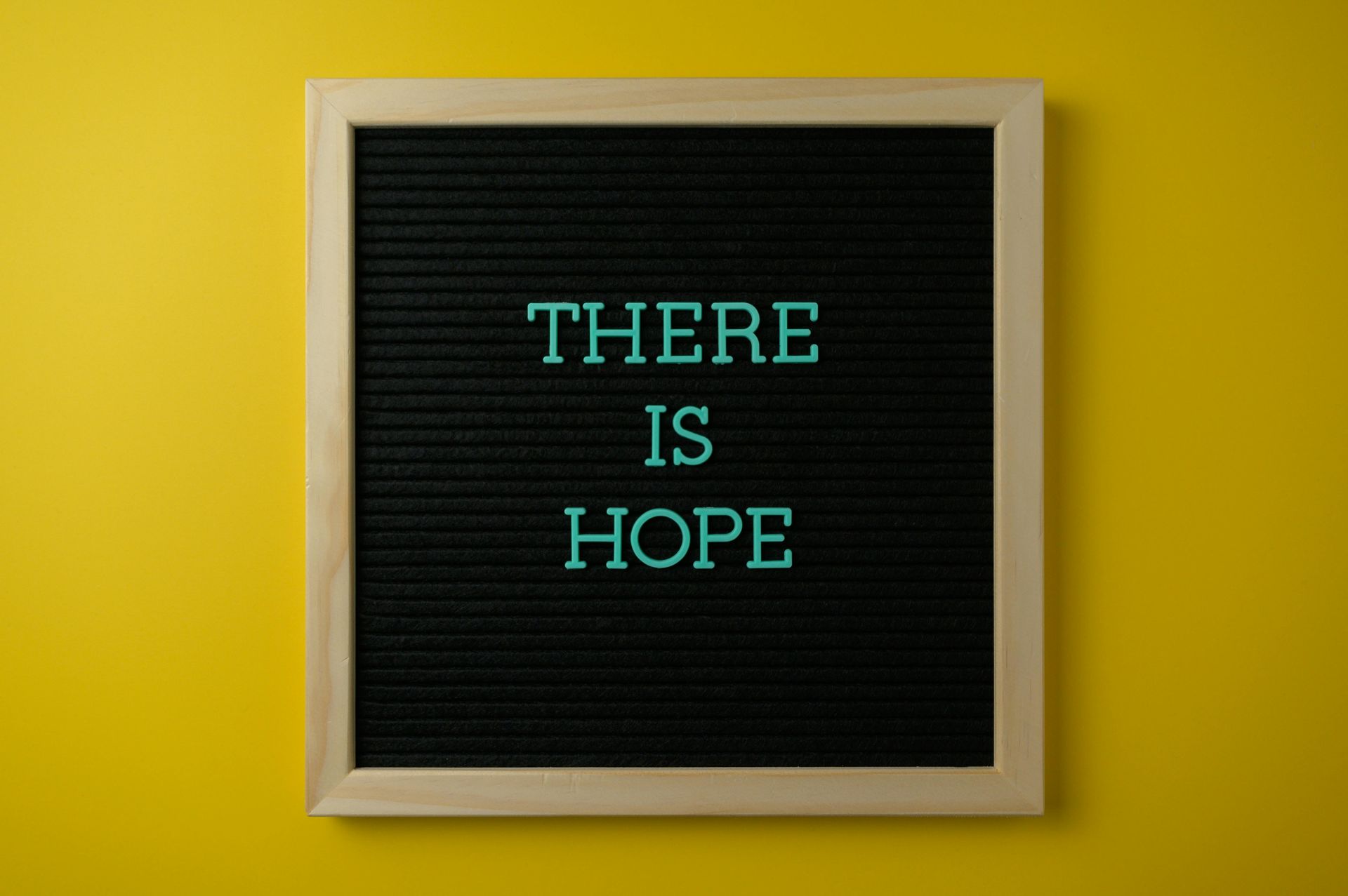 Framed black letter board on a yellow wall reading “THERE IS HOPE” in teal letters