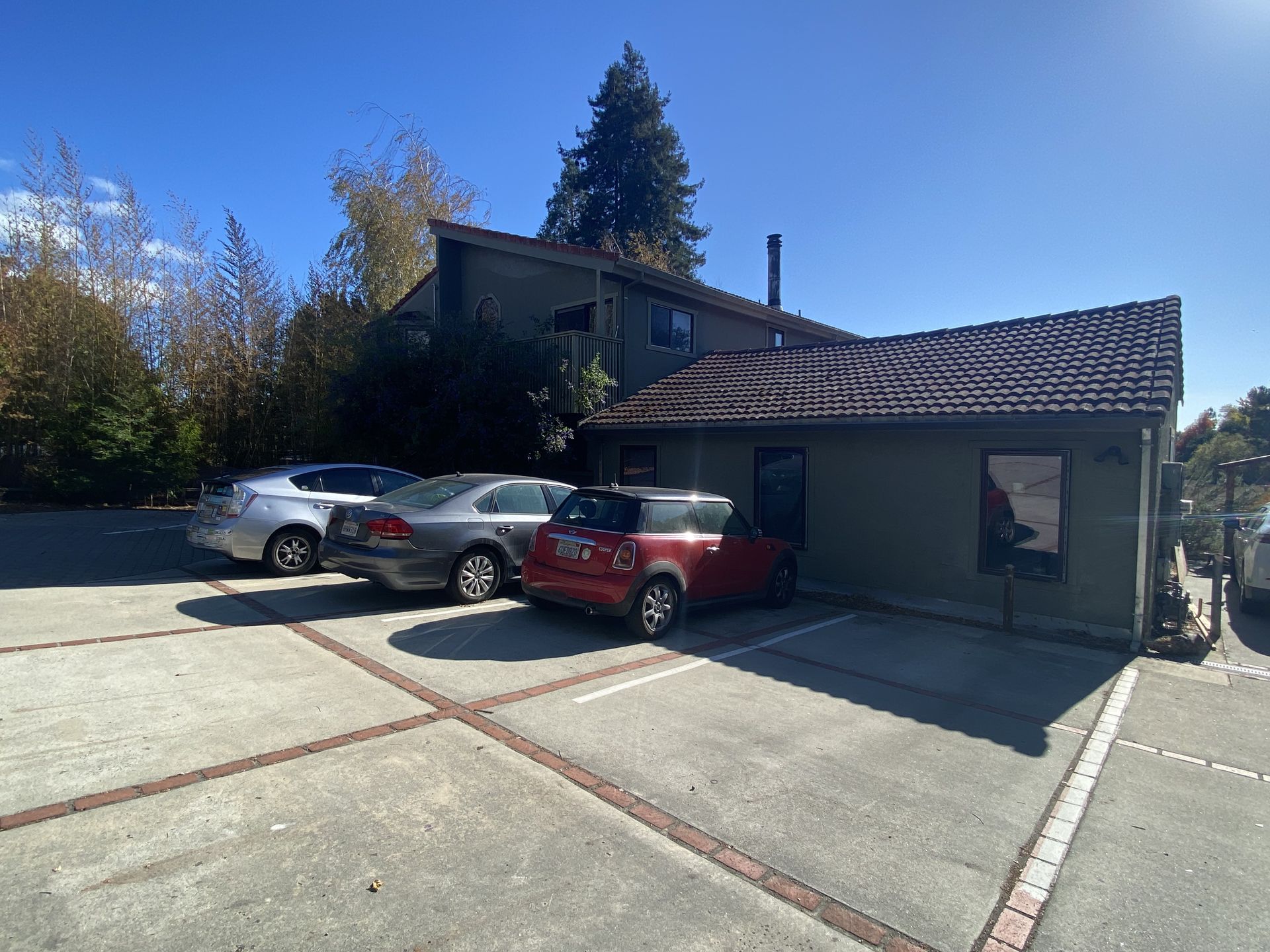 Cars parked outside a two-story building with a brown tiled roof under a sunny blue sky.