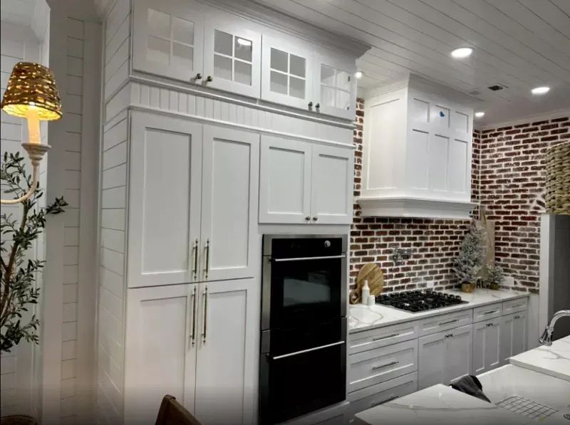 A kitchen with white cabinets , a black oven , and a brick wall.