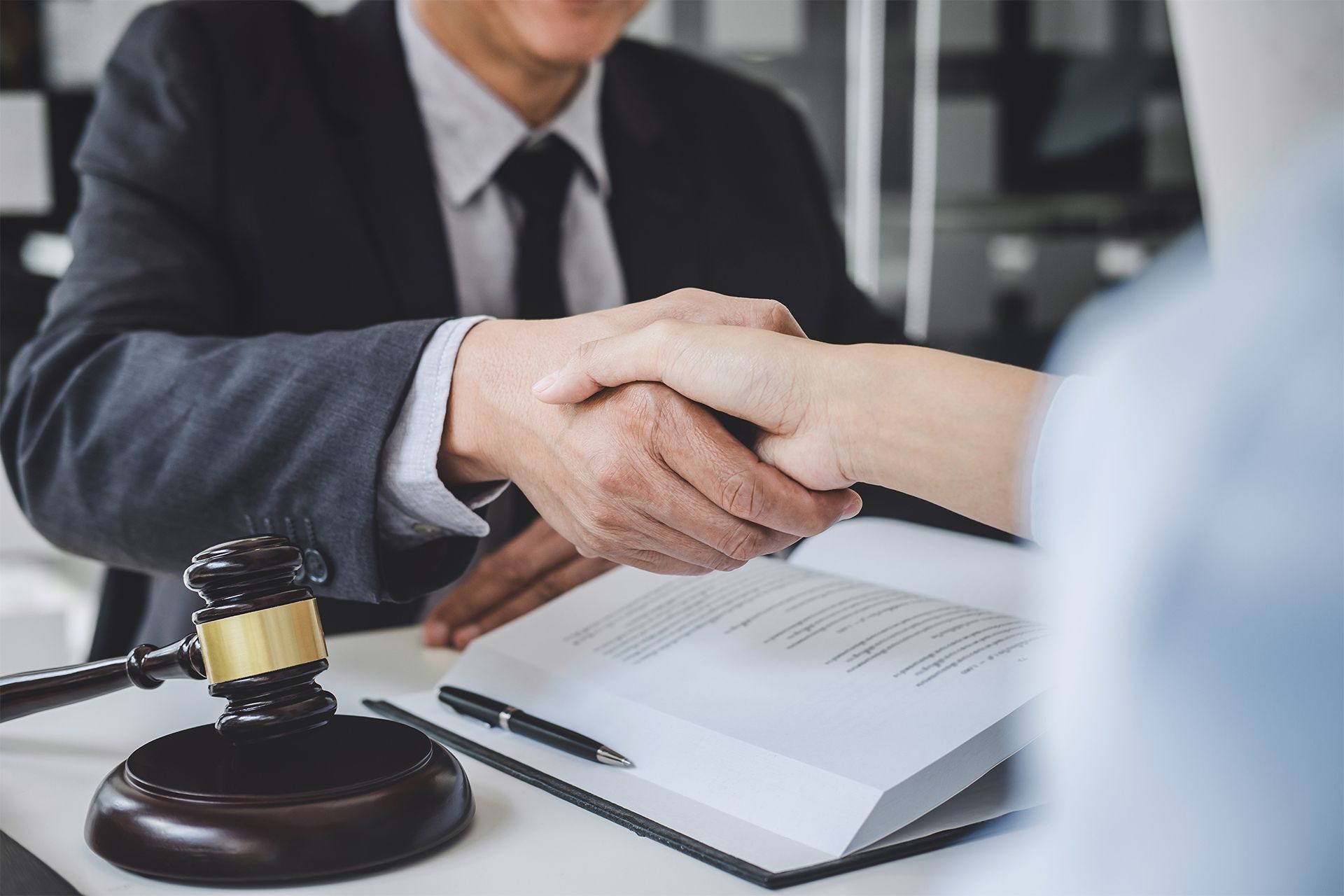 Handshake between a lawyer in a suit and another person, beside a gavel and open book.