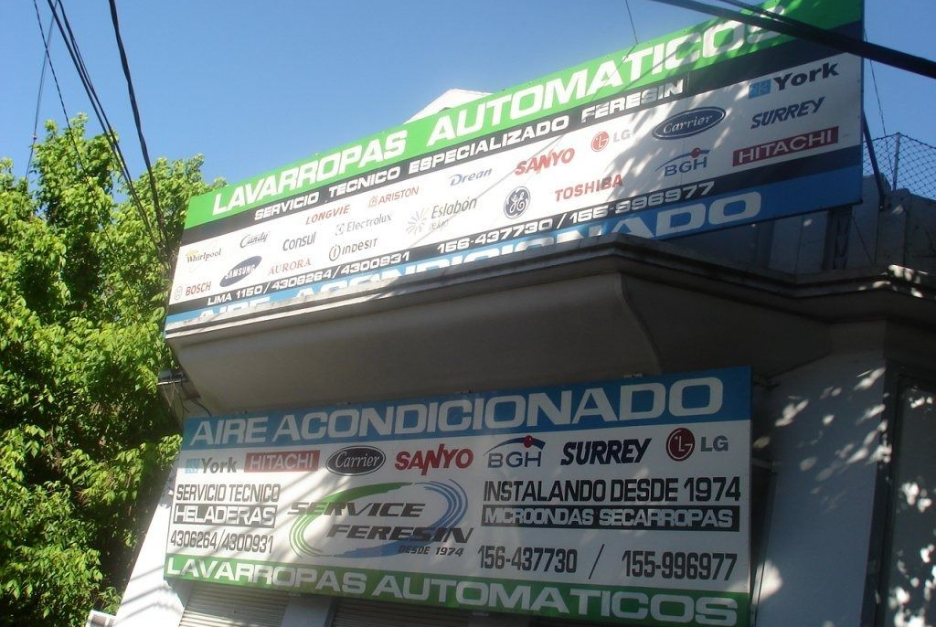 Letrero de taller de reparación y aire acondicionado automotriz en una esquina soleada.