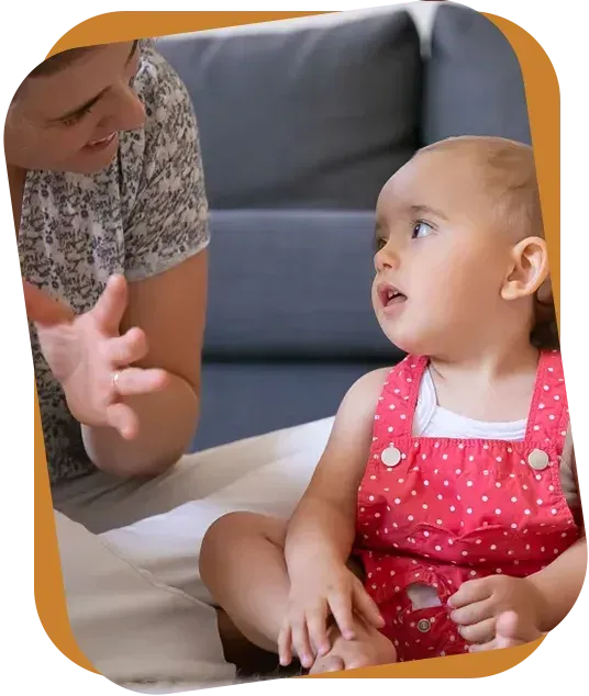 An RBT shows three flashcards featuring clothing items to a child sitting on a rug in a bright room.