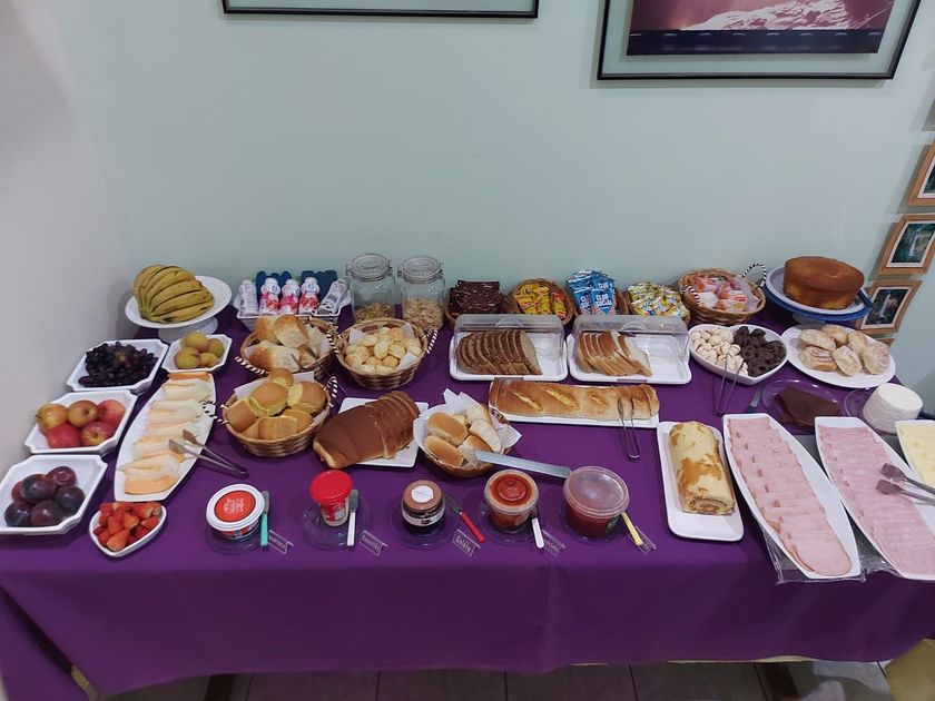 Mesa de bufê com vários tipos de doces, potes e petiscos sobre uma toalha de mesa amarela, em uma sala de jantar.