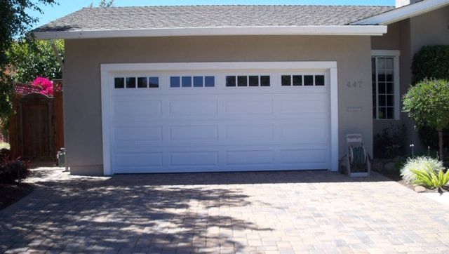 Single-story house with a white garage door and driveway in bright sunlight