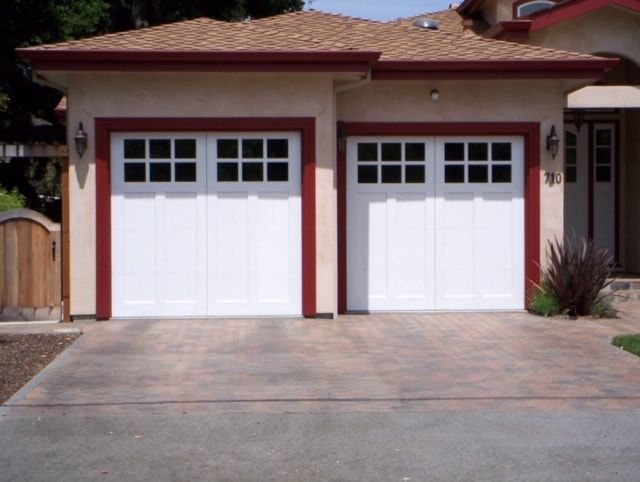 Two white garage doors on a beige house with a paved driveway