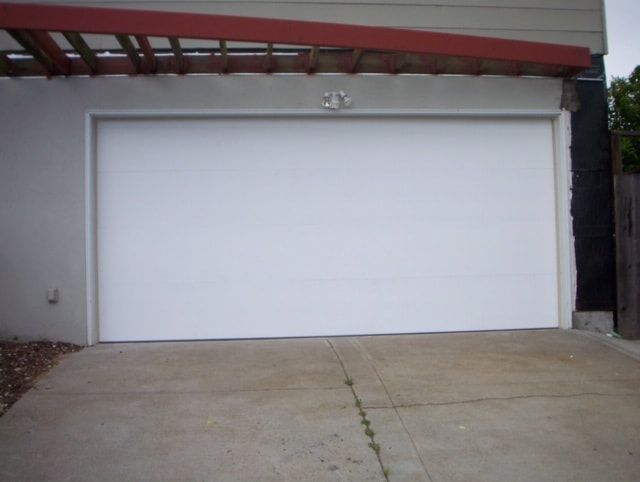 White garage door on a concrete driveway under a carport-like overhang