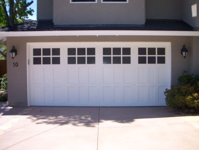 White two-car garage door on a house exterior with driveway and wall-mounted lights