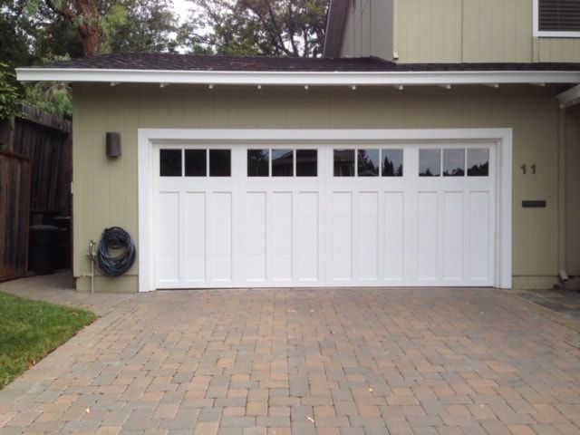White garage door with small windows on a brick driveway beside a beige house
