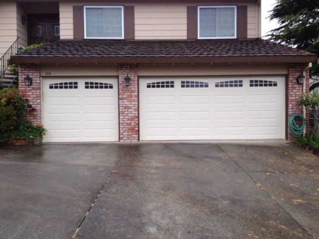 Suburban two-car garage with white doors and a wet driveway in front of a house