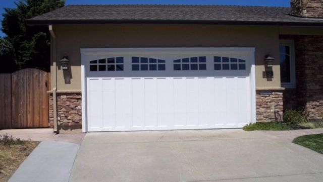 Single-car garage with white door and windows, front of a suburban house with driveway and brick trim.