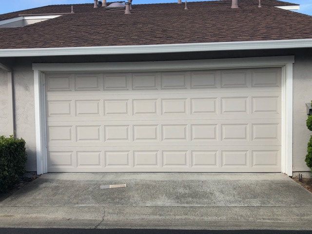 Closed beige two-car garage door with driveway in front of a house