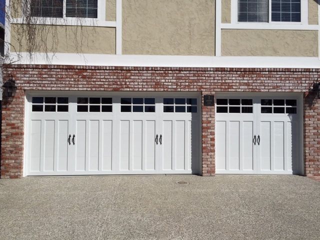 Two white garage doors in a brick-and-stucco house exterior