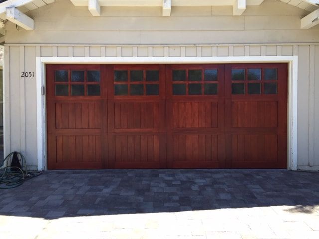Red wooden garage door with small windows in a beige house exterior.