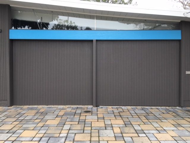 Modern storefront with closed gray shutters, blue awning, and tiled pavement in front