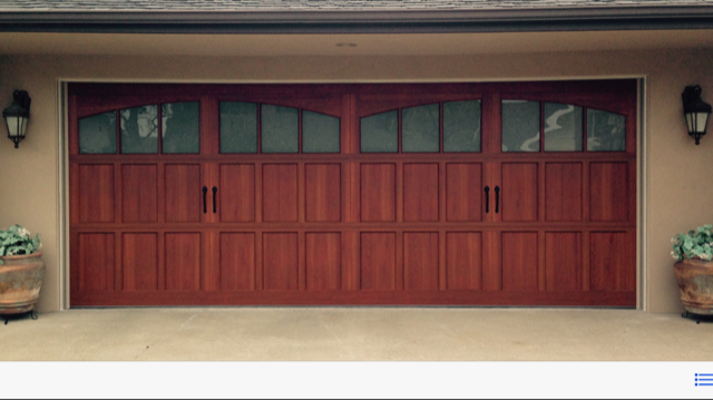 Red wooden double garage door with arched windows on a beige house exterior