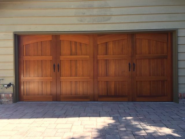 Wooden four-car garage door on a house exterior with a paved driveway in front.