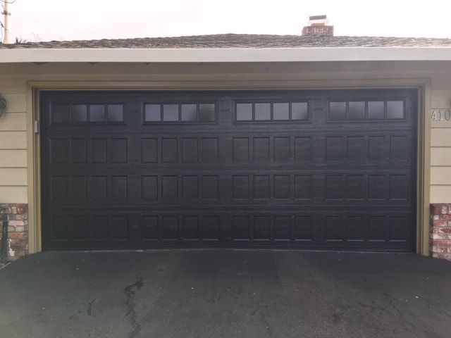 Closed black garage door with dark driveway in front of a beige building