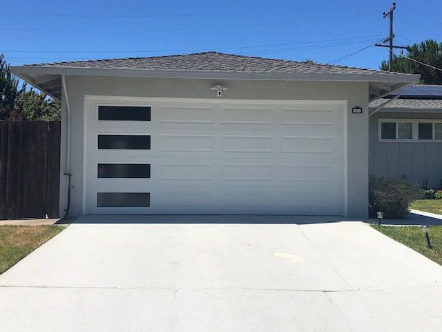 Modern white garage with four dark window panels, long driveway, and blue sky overhead