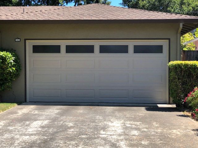 Single-car garage with a closed white door and concrete driveway in front of a house