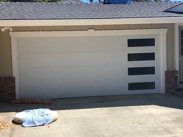 Modern white garage door with three narrow windows and a covered object on the driveway
