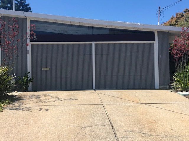 Modern gray garage with two doors and a sloped concrete driveway under a clear blue sky