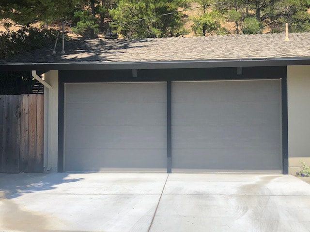 Closed gray two-car garage doors with a concrete driveway and trees above the roofline