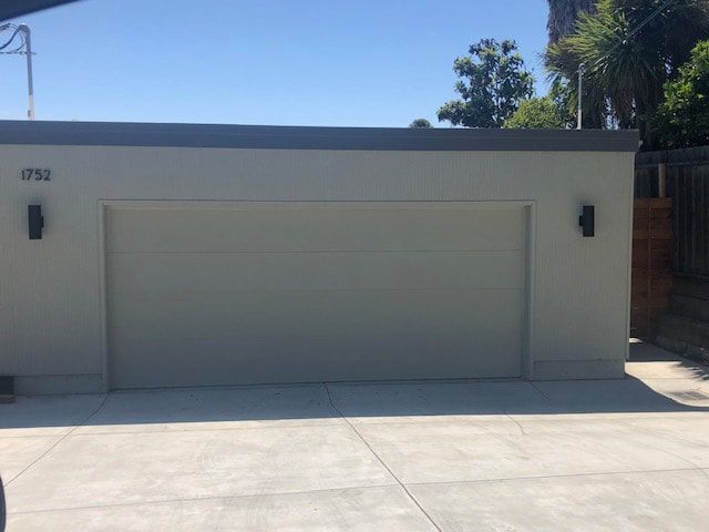 Closed gray garage door on a white house with driveway and bright blue sky