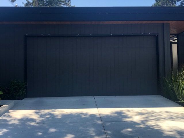Modern black garage door on a contemporary house with a concrete driveway and blue sky.