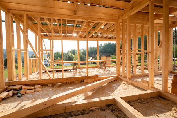 Unfinished wooden frame of a house interior with exposed beams and views of the surrounding landscape.