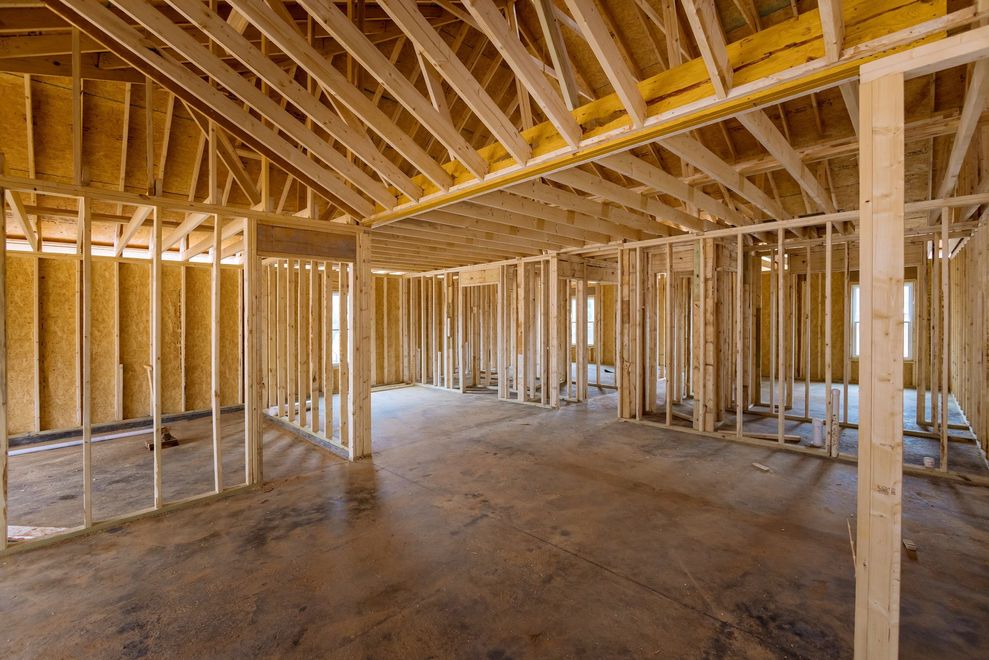 Interior view of a residential building under construction with exposed wooden wall framing and roof trusses.