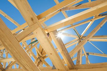 Wooden roof trusses of a house under construction silhouetted against a bright blue sky with the sun shining through.